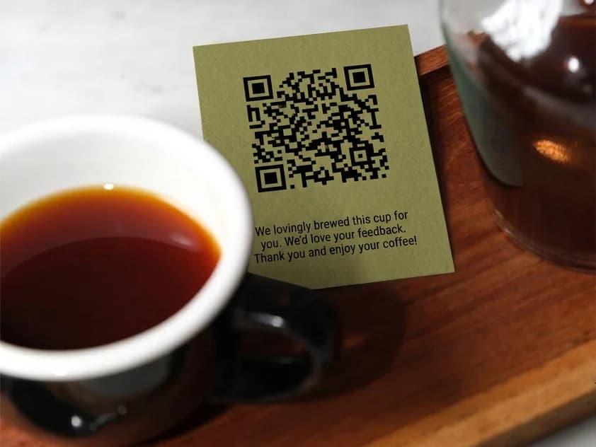 A QR card standing next to a cup of filter coffee on a wooden tray